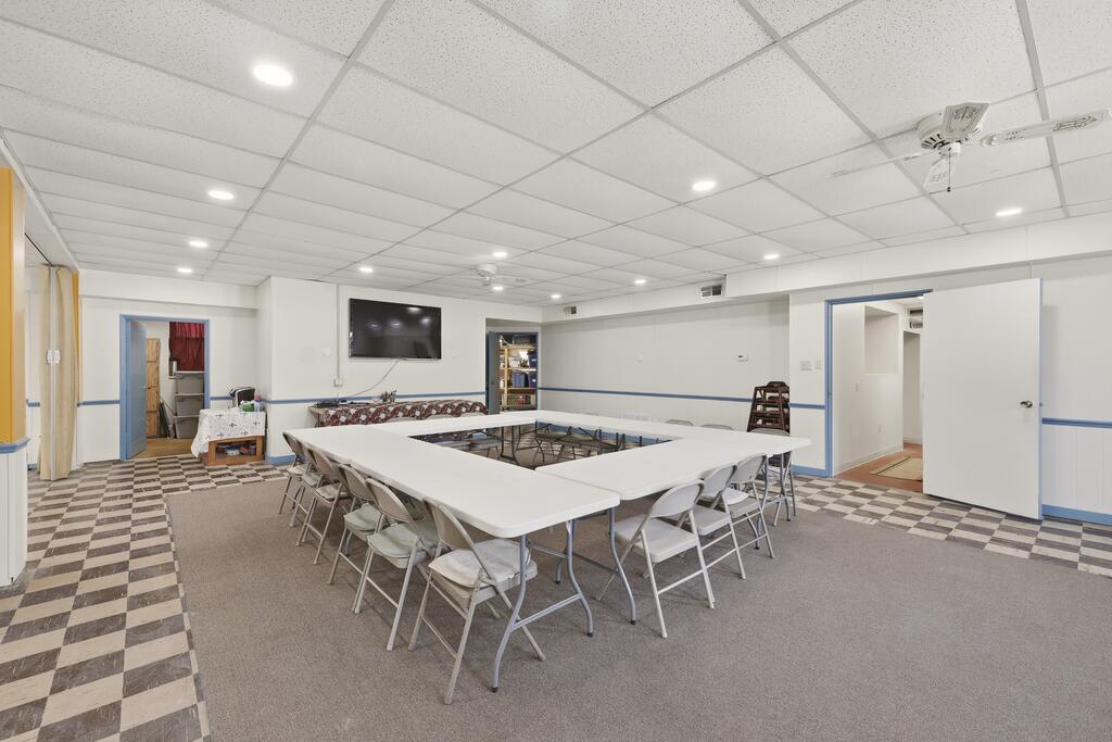 Meeting room with tables arranged in a square, folding chairs, checkerboard tile, and a wall-mounted television.