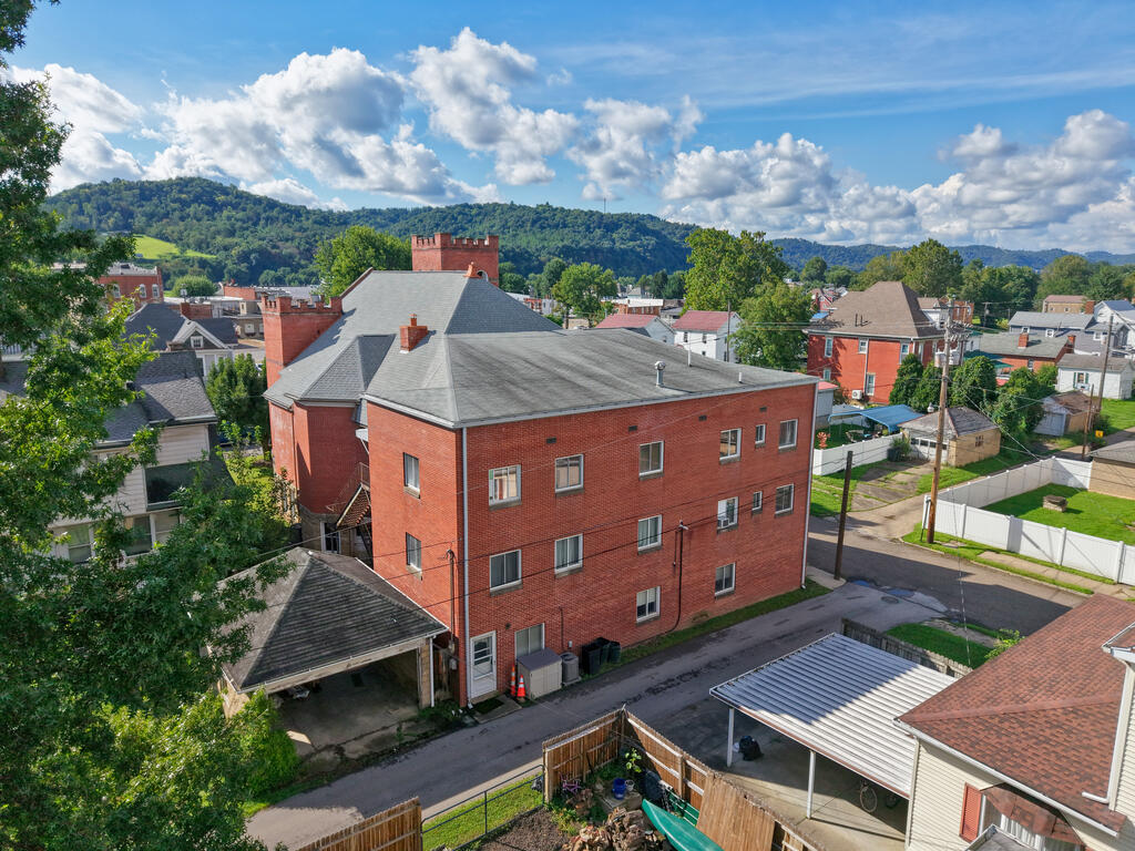 Aerial view of a red-brick building among neighborhood homes, with wooded hills in the distance.