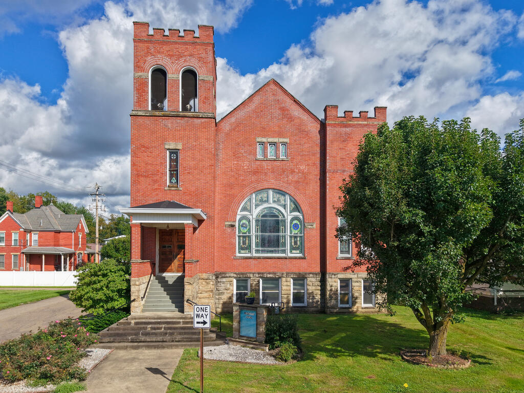 Red-brick building with crenellated towers, an arched stained-glass window, and front steps.