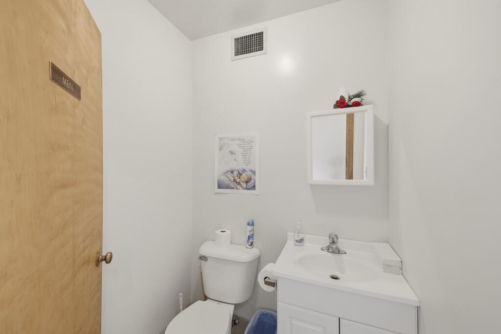 Bathroom with a white toilet, vanity sink, mirrored cabinet, and wooden door marked “MEN.”