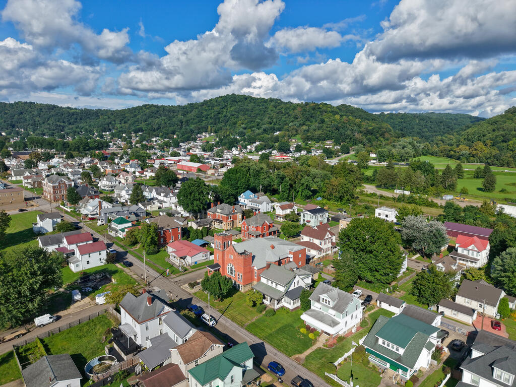 Aerial view of a small town with a red-brick church, wooded hills, and green fields.