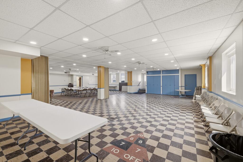 Multipurpose room with a checkerboard floor, folding tables, and rows of chairs.