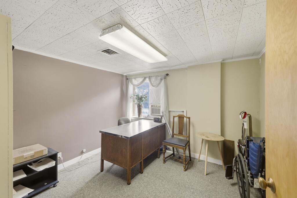 Office with a wooden desk, chair, and wheelchair beside a curtained window.