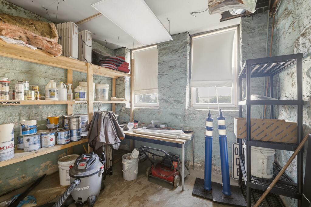 Unfinished workshop with paint-filled shelves, a worktable, and a wet/dry vacuum