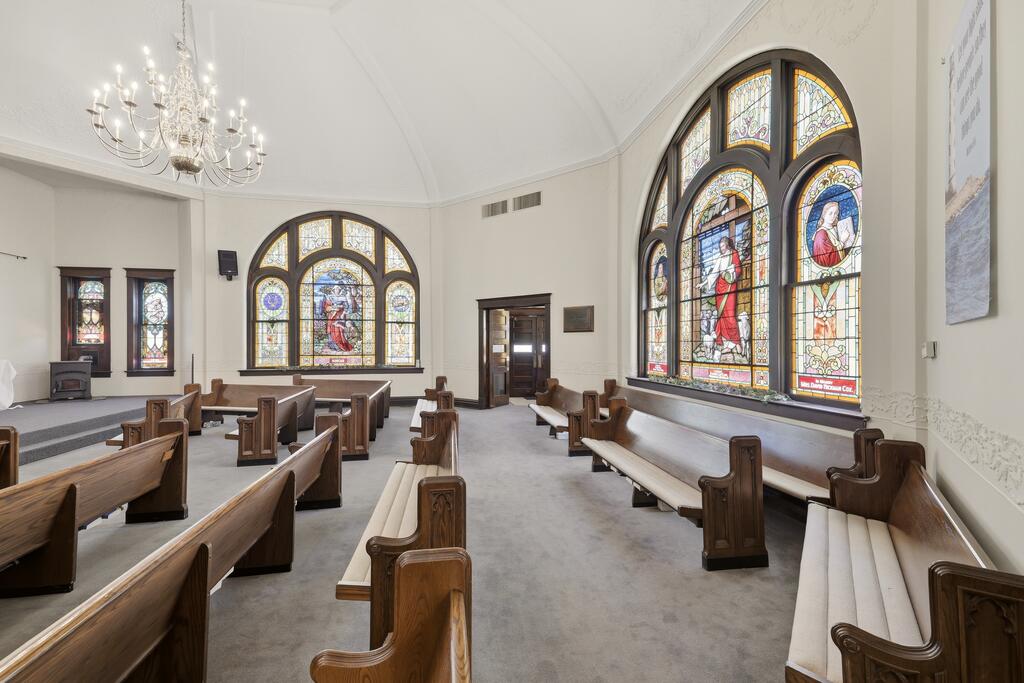 Sanctuary with wooden pews and large arched stained-glass windows.
