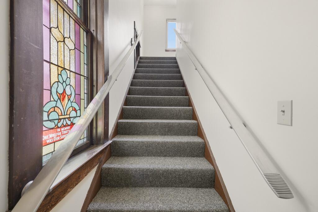 Carpeted staircase beside a tall stained-glass memorial window.