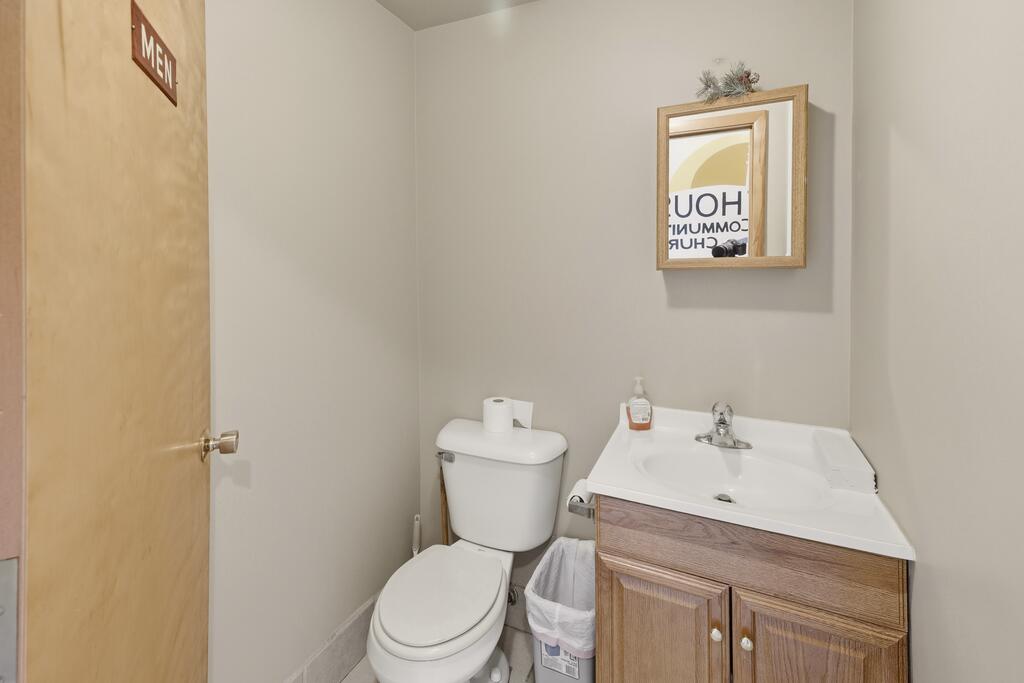 Bathroom with a white toilet, wood vanity, framed mirror, and MEN sign on the door.