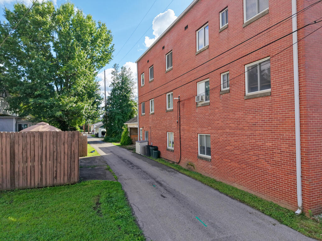Red brick building beside an asphalt driveway, with a wooden fence and mature trees.