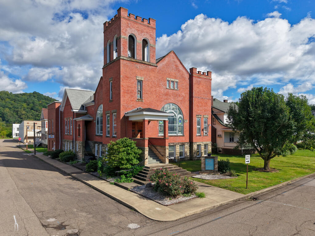 Red-brick building with a tall tower and arched stained-glass windows on a landscaped corner lot.