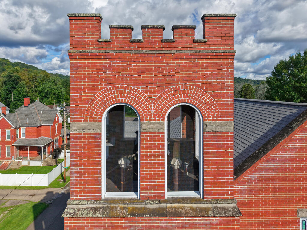 Red brick facade with two arched windows and a crenellated parapet above a slate roof.