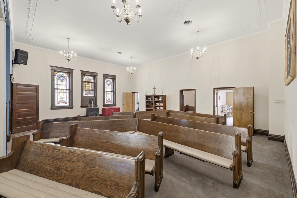 Chapel sanctuary with wooden pews, stained-glass windows, and chandeliers.