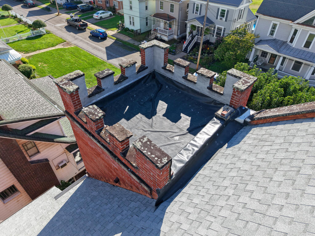 Aerial view of a flat roof surrounded by brick chimneys and neighboring homes.