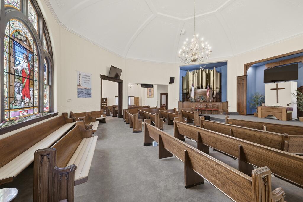 Church sanctuary with wooden pews, stained-glass windows, and pipe organ.
