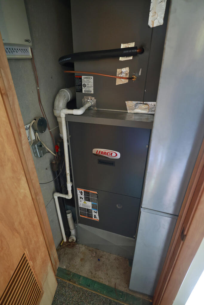 Lennox furnace and HVAC equipment in a narrow utility closet with exposed pipes.