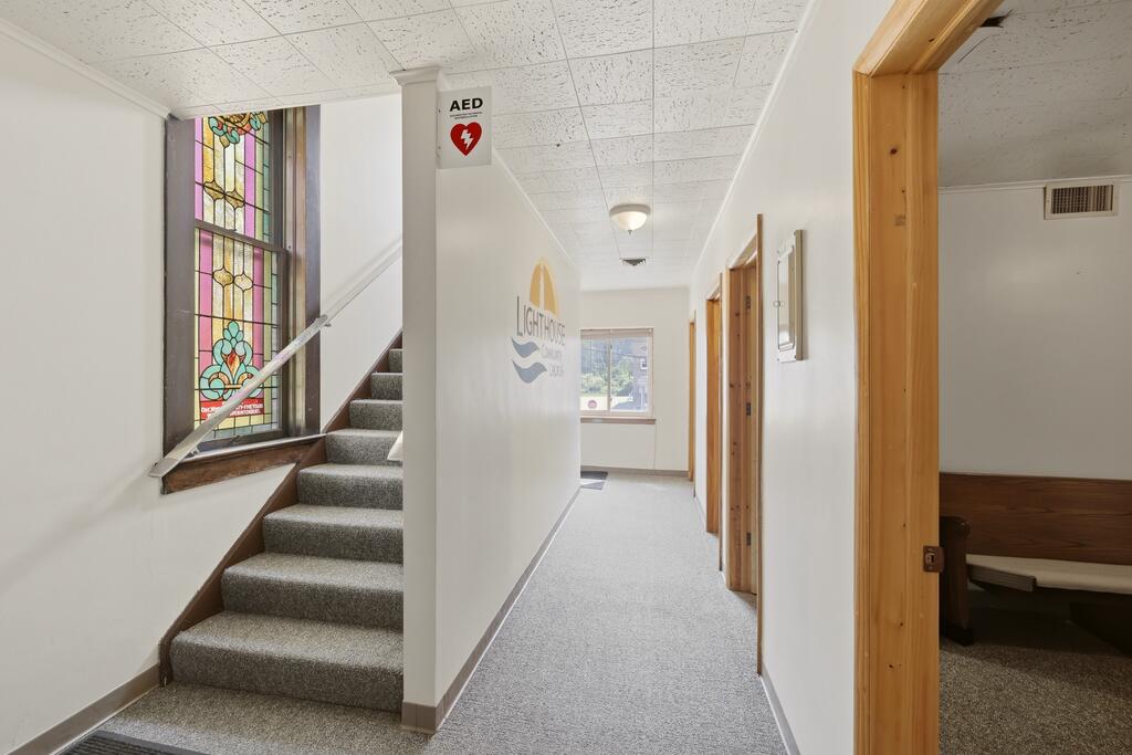Hallway with a carpeted staircase beside a colorful stained-glass window and an open doorway.