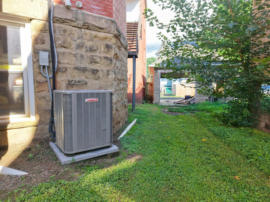 Side yard with a Lennox air-conditioning unit beside a stone foundation and grassy lawn.