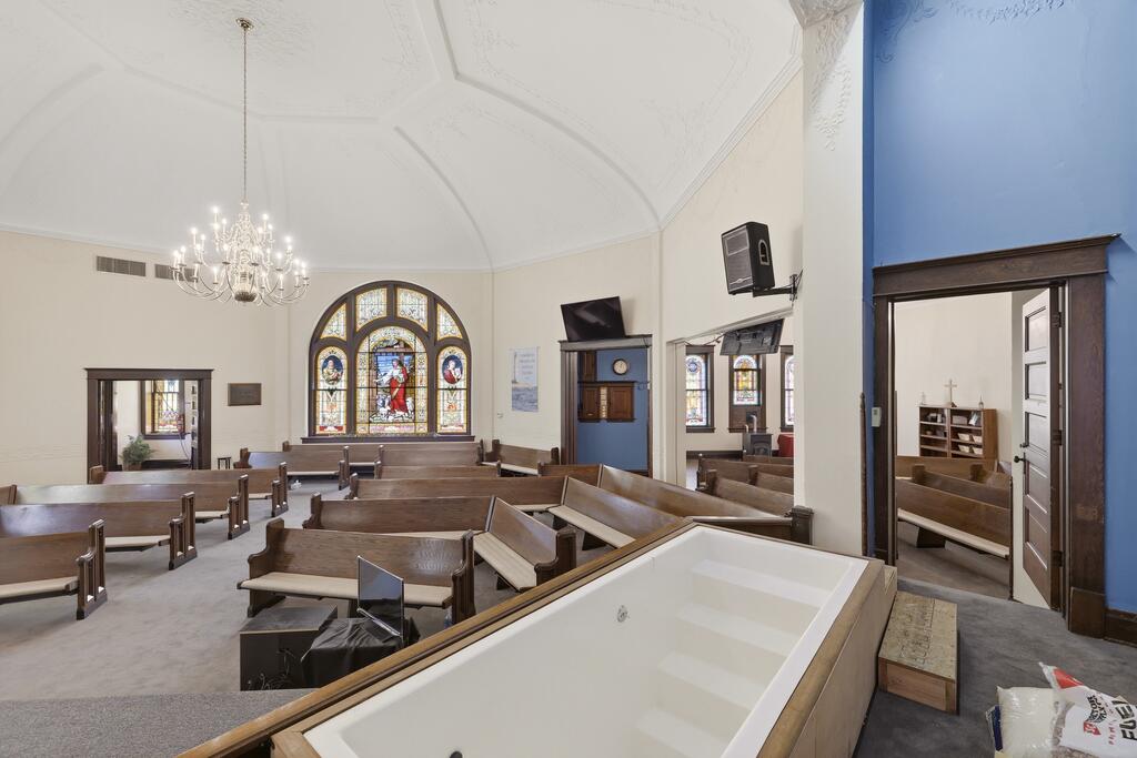 Church sanctuary with wooden pews, a large stained-glass window, and a baptismal font.