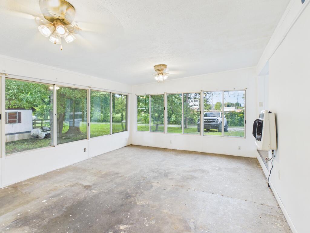 Empty sunroom with large windows, two ceiling fans, and a bare concrete floor.