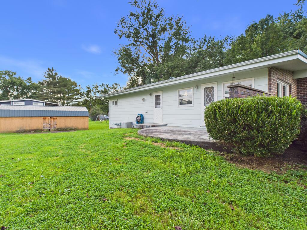 Rear of a single-story home with a concrete patio, trimmed hedge, and detached shed.
