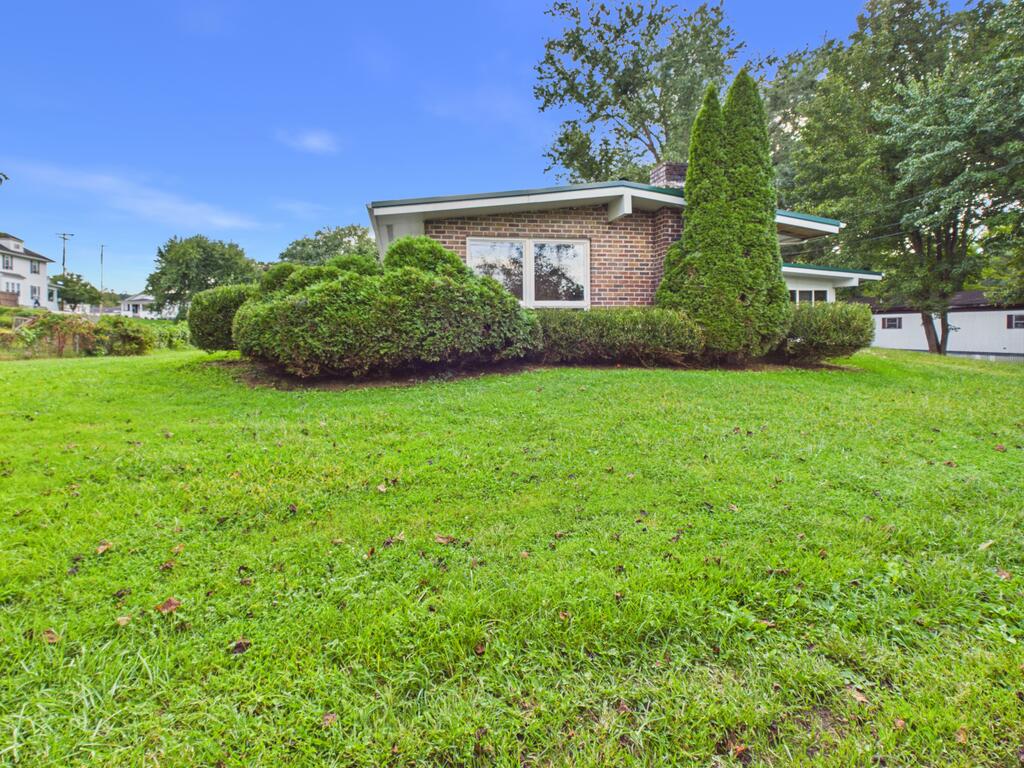 Single-story brick house behind a broad lawn and neatly trimmed shrubs.
