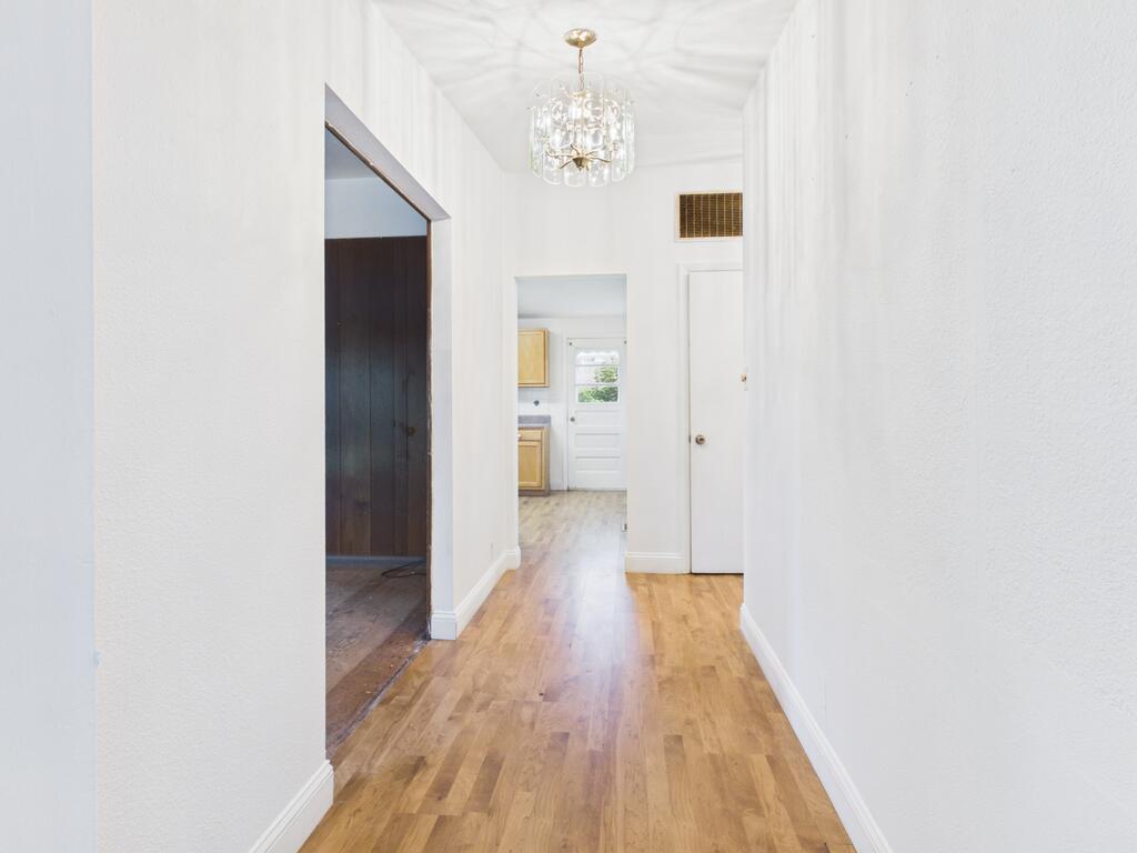 Hallway with warm wood flooring, white walls, and a chandelier.