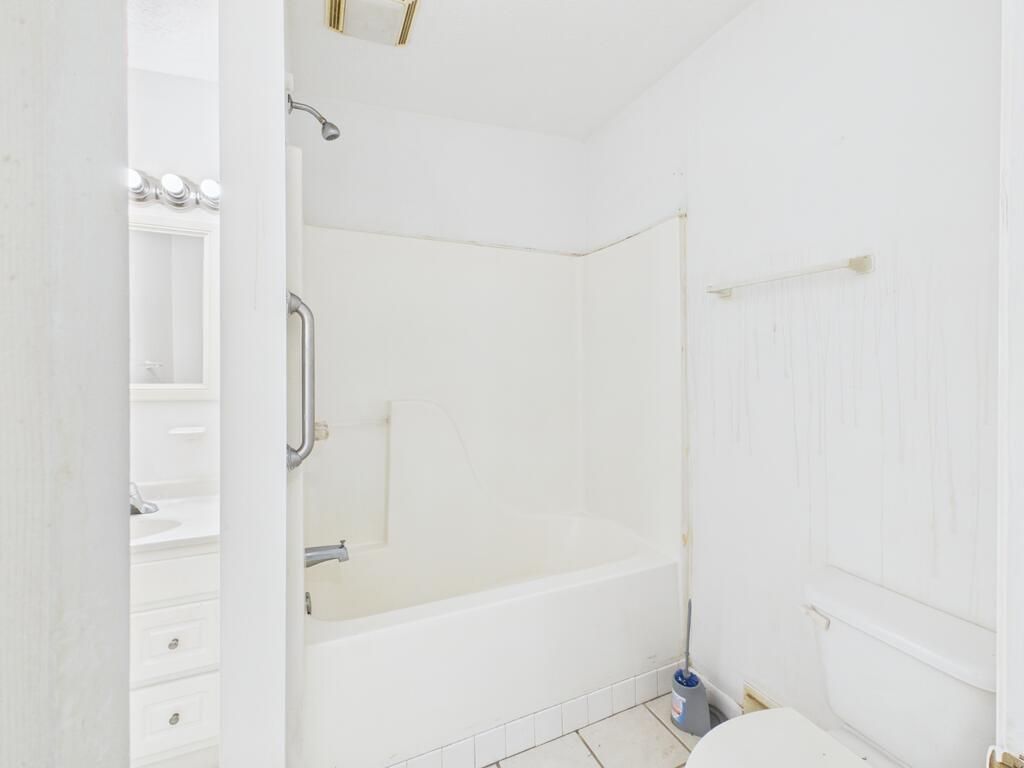 White bathroom with a tub-shower, grab bar, toilet, and vanity.