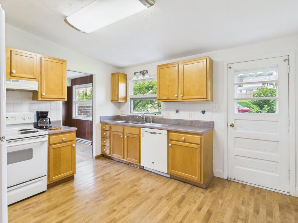 Kitchen with honey-colored cabinets, white appliances, and a door to the outside.