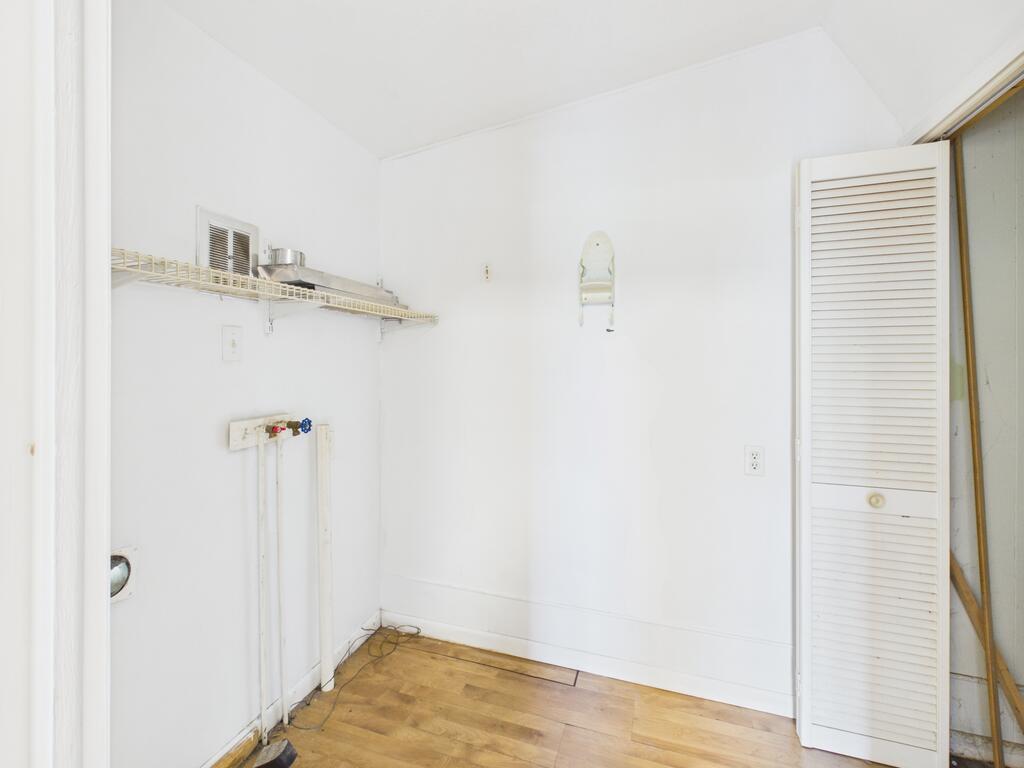 Empty utility room with exposed washer hookups, a wire shelf, and wood-pattern flooring.