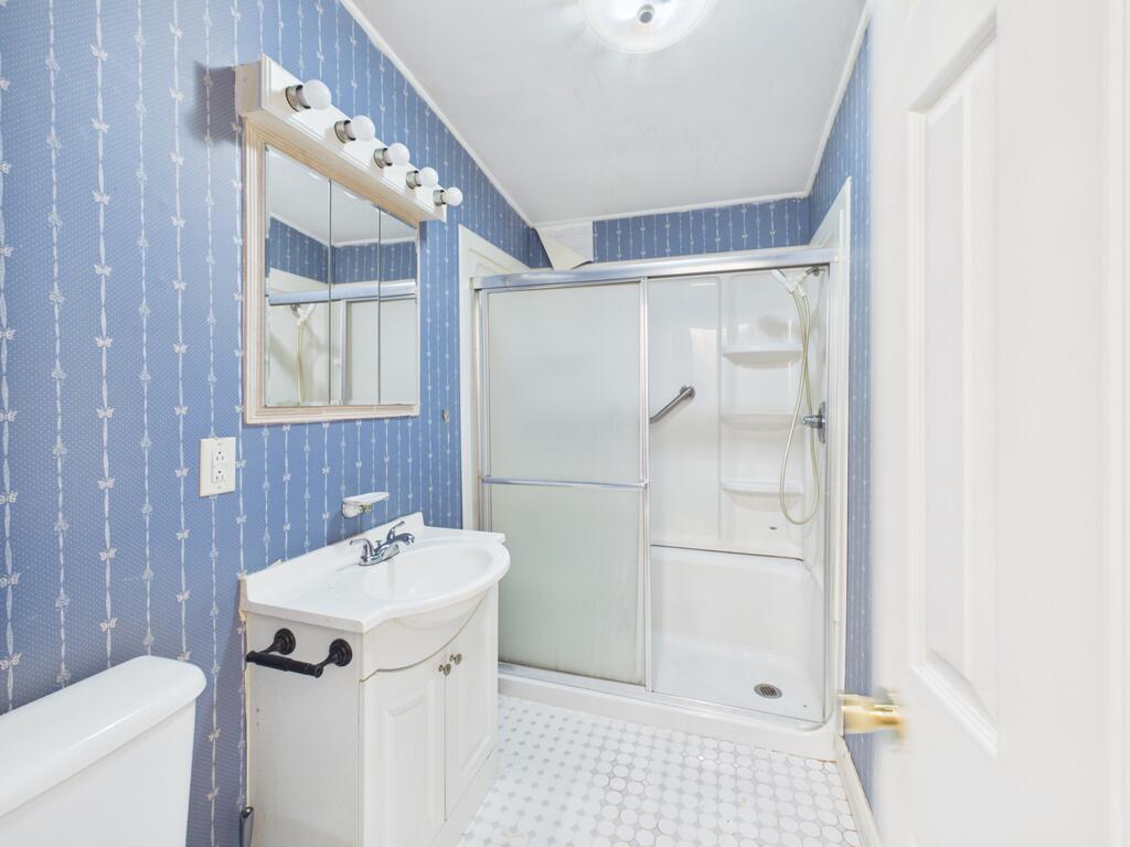 Bathroom with blue patterned wallpaper, white vanity, and glass-enclosed shower.