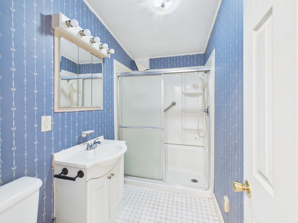 Bathroom with blue patterned wallpaper, white vanity, and sliding glass shower enclosure.