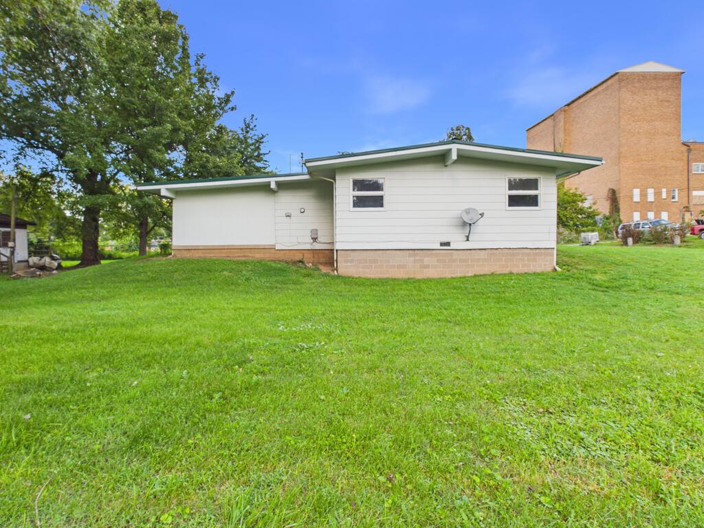 Single-story white house with a tan brick foundation and satellite dish beside a broad green lawn.
