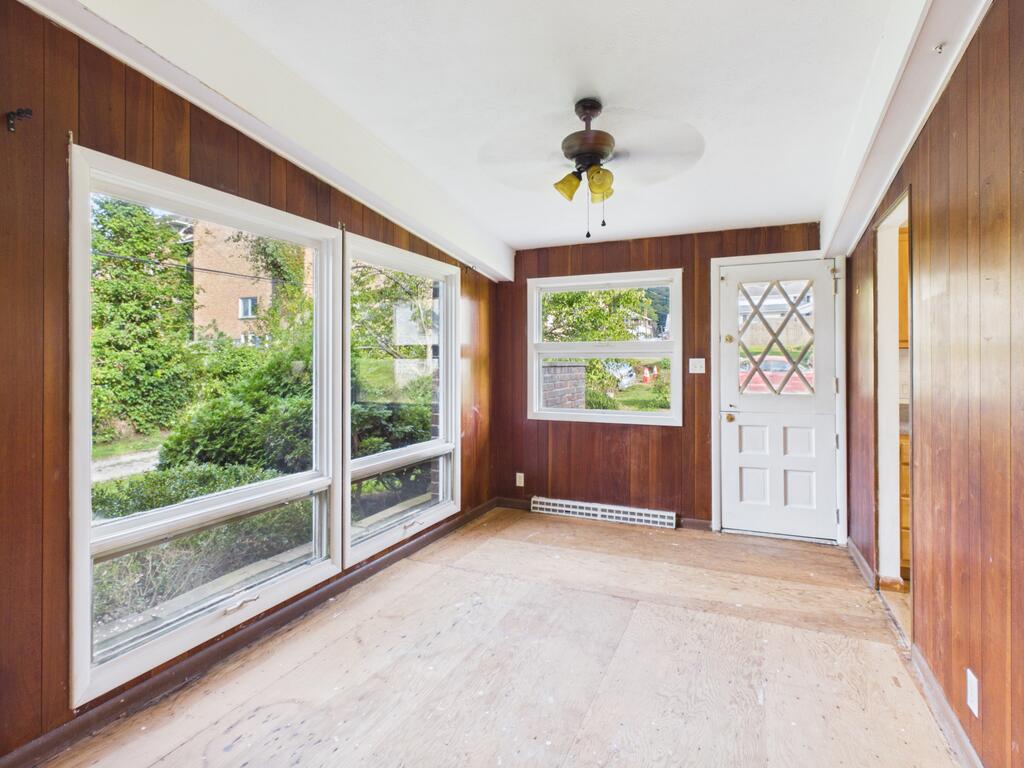 Empty sunroom with wood-paneled walls, broad windows, and a white exterior door.