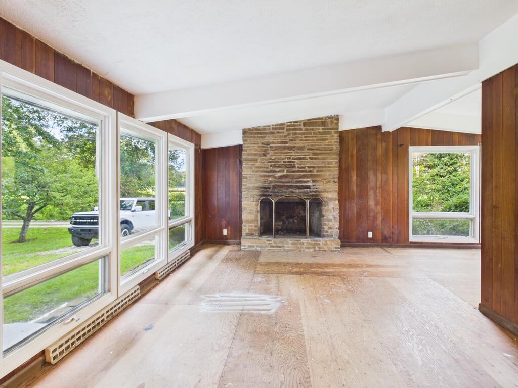 Vacant living room with a stone fireplace, wood-paneled walls, and large windows.