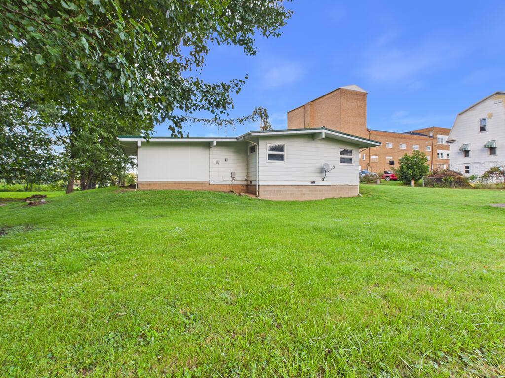 Rear of a white single-story house with a satellite dish, wide lawn, and leafy tree.