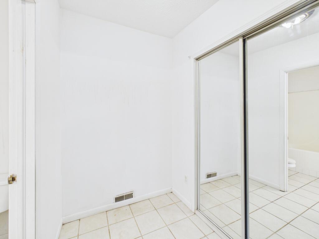 Empty tiled room with mirrored sliding closet doors and a bathroom visible in the reflection.