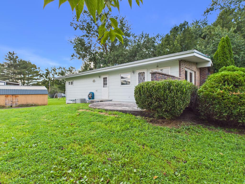 Single-story white-sided home with a brick section, concrete patio, and broad lawn.