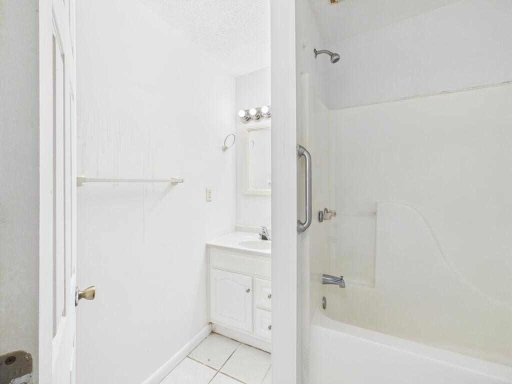 Bathroom with a white bathtub and shower beside a vanity and mirror.