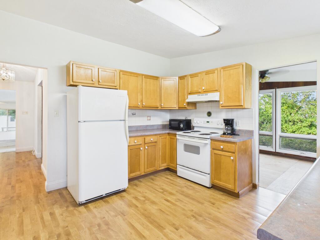 Kitchen with honey-colored cabinets, white appliances, laminate flooring, and a large window overlooking greenery.