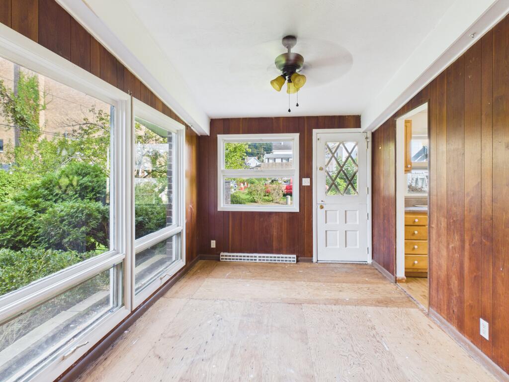 Unfurnished sunroom with wood-paneled walls, large windows, and a bare plywood floor.