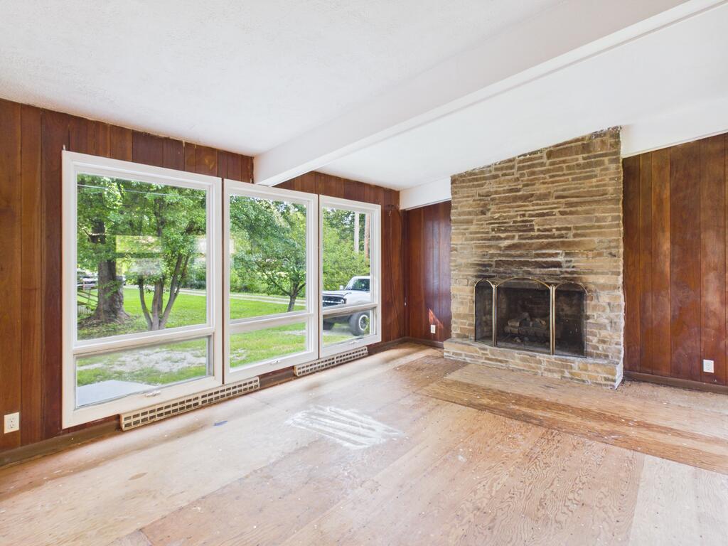 Living room with a stone fireplace, broad windows, and wood-paneled walls.