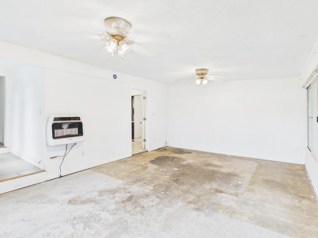 Vacant room with white walls, two ceiling fans, a wall heater, and a stained concrete floor.