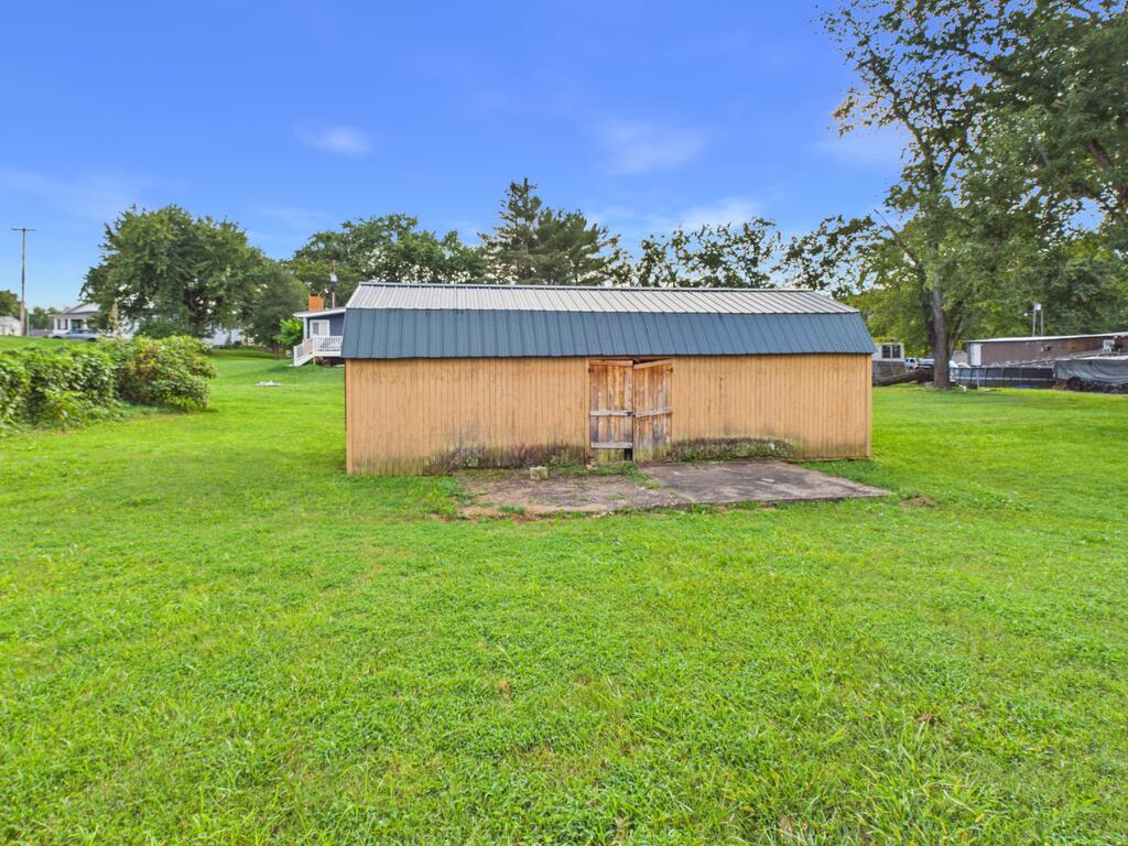 Detached wooden outbuilding with a gray metal roof and weathered doors in a grassy yard.