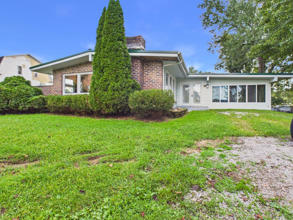 Single-story brick home with a white-sided addition, tall evergreen, and front lawn.