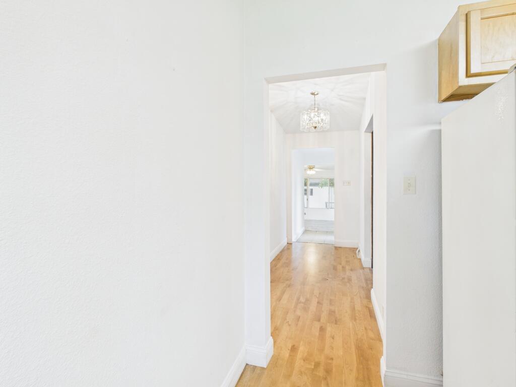 Bright hallway with light wood floors, a chandelier, and open doorways leading to a sunlit room.