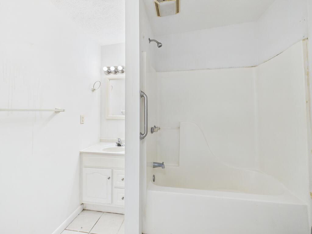 Bathroom with a white tub and shower, grab bar, and vanity.