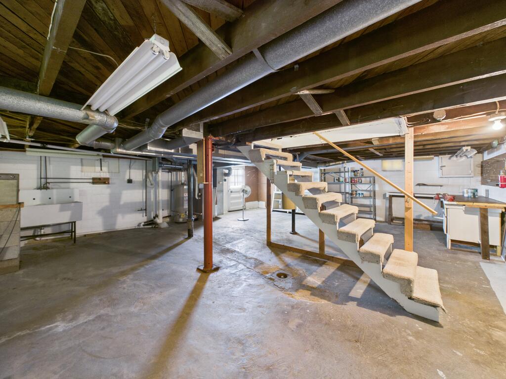 Unfinished basement with exposed ductwork and joists, concrete floor, and carpeted stairs.