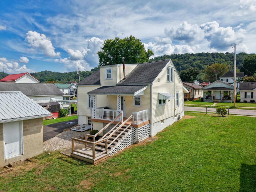 Pale yellow house with a raised wooden deck and stairs opening onto a grassy yard.