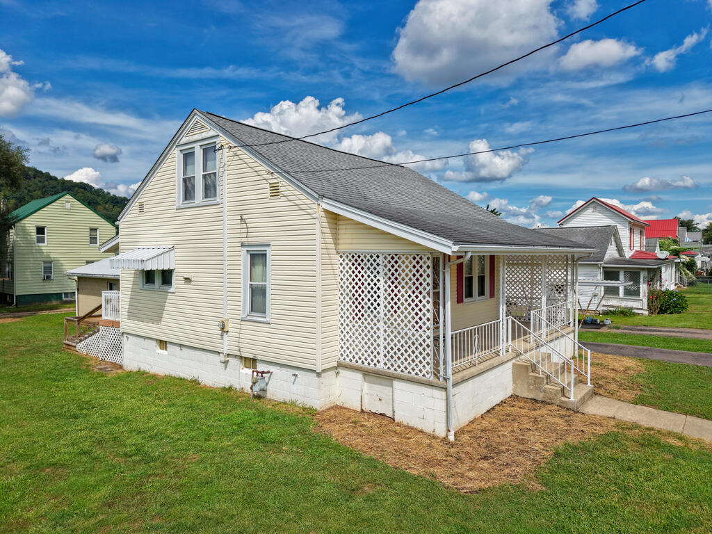 Beige gable-roofed house with a lattice-covered porch and white steps beside a green lawn.