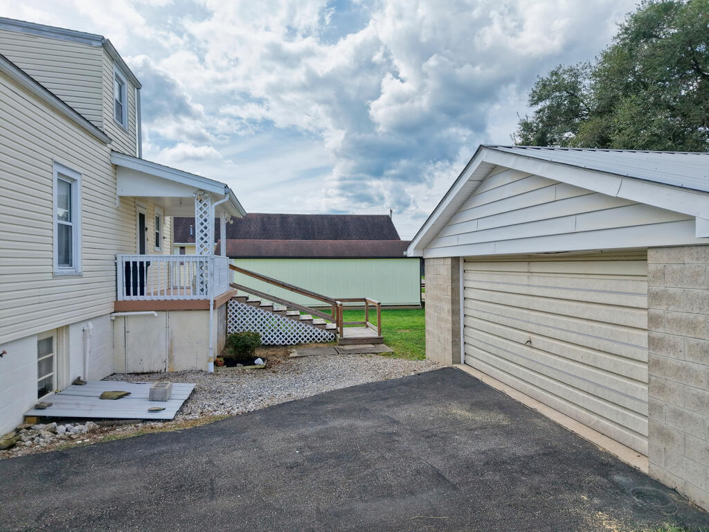 House and detached garage flank a paved driveway; a wooden ramp leads to the porch.