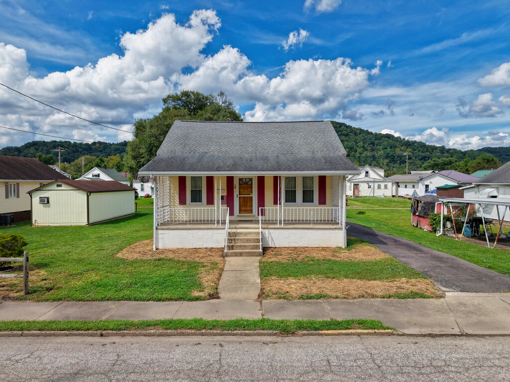 Small house with red shutters and a covered porch, viewed from the street.